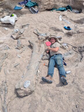 man lying next to large dinosaur bone